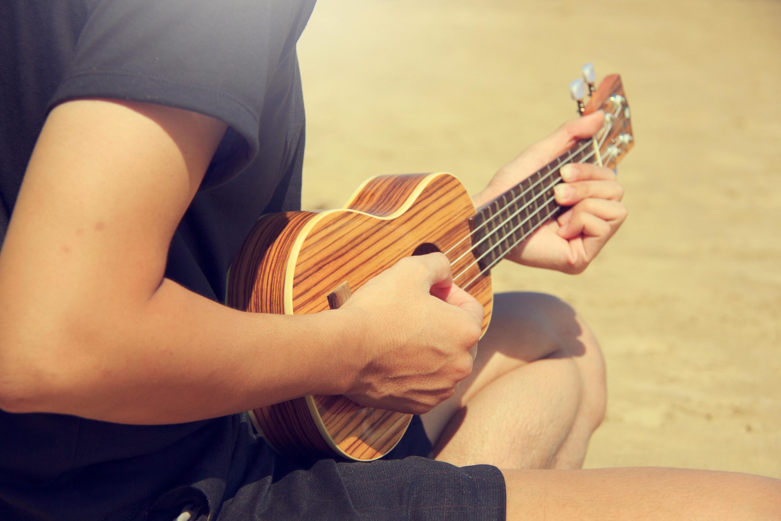 Close-up of a man playing ukulele on a sunny beach with soft, natural lighting.