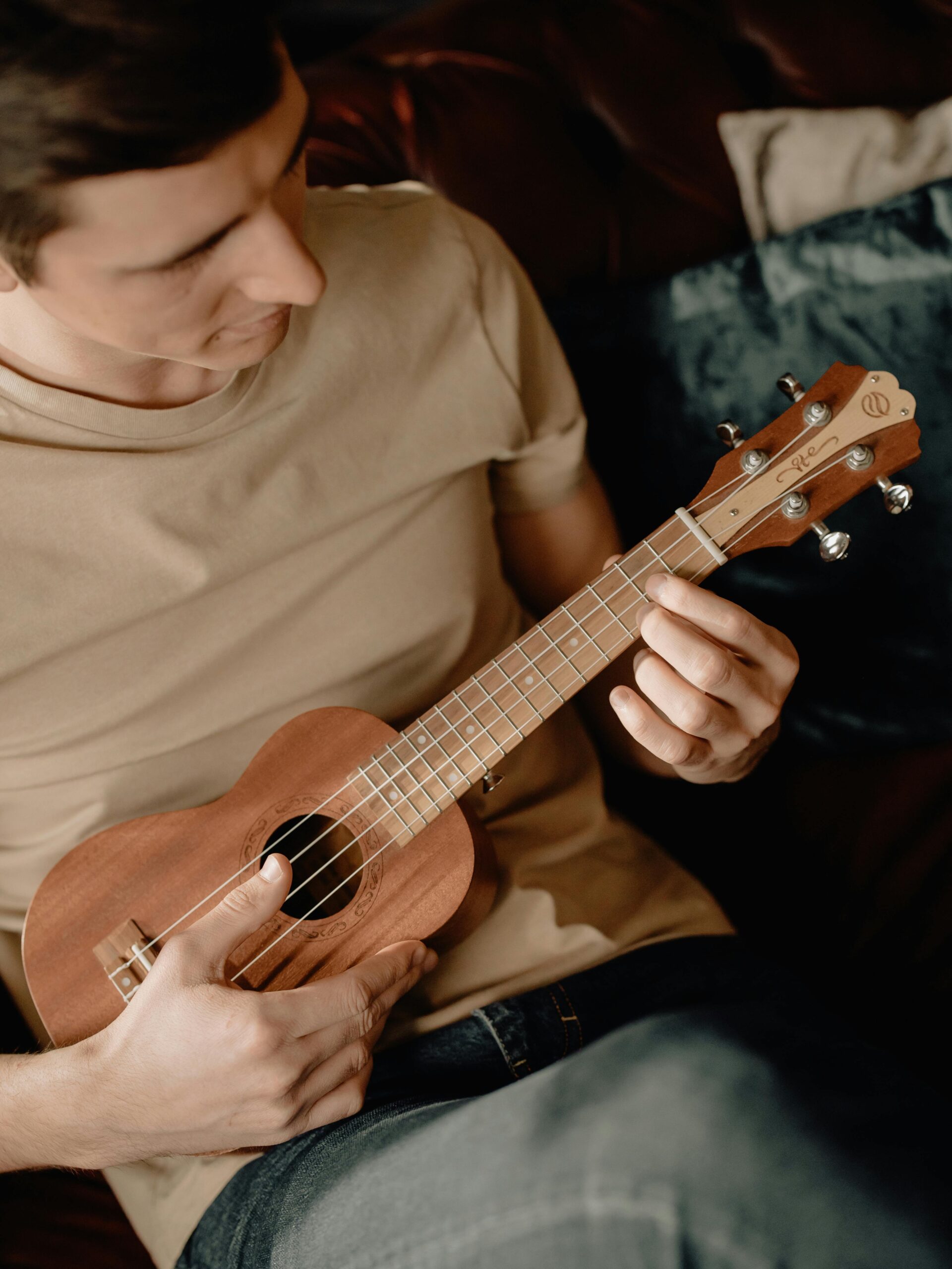 A young man plays the ukulele in a cozy home setting, focused on the music.