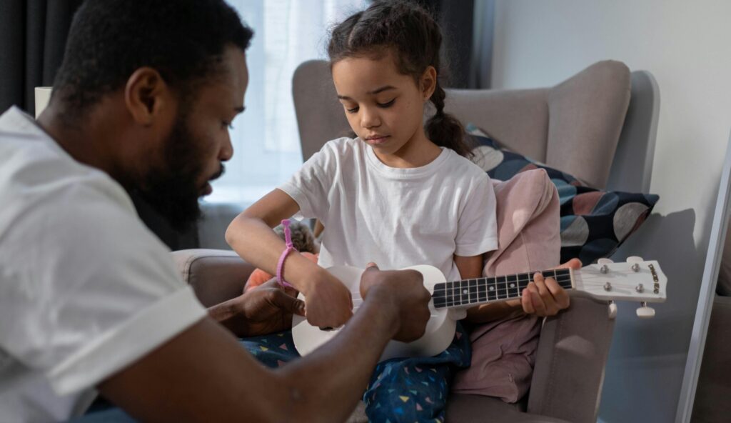 A father and daughter bonding indoors while learning to play the ukulele, creating a warm family moment.