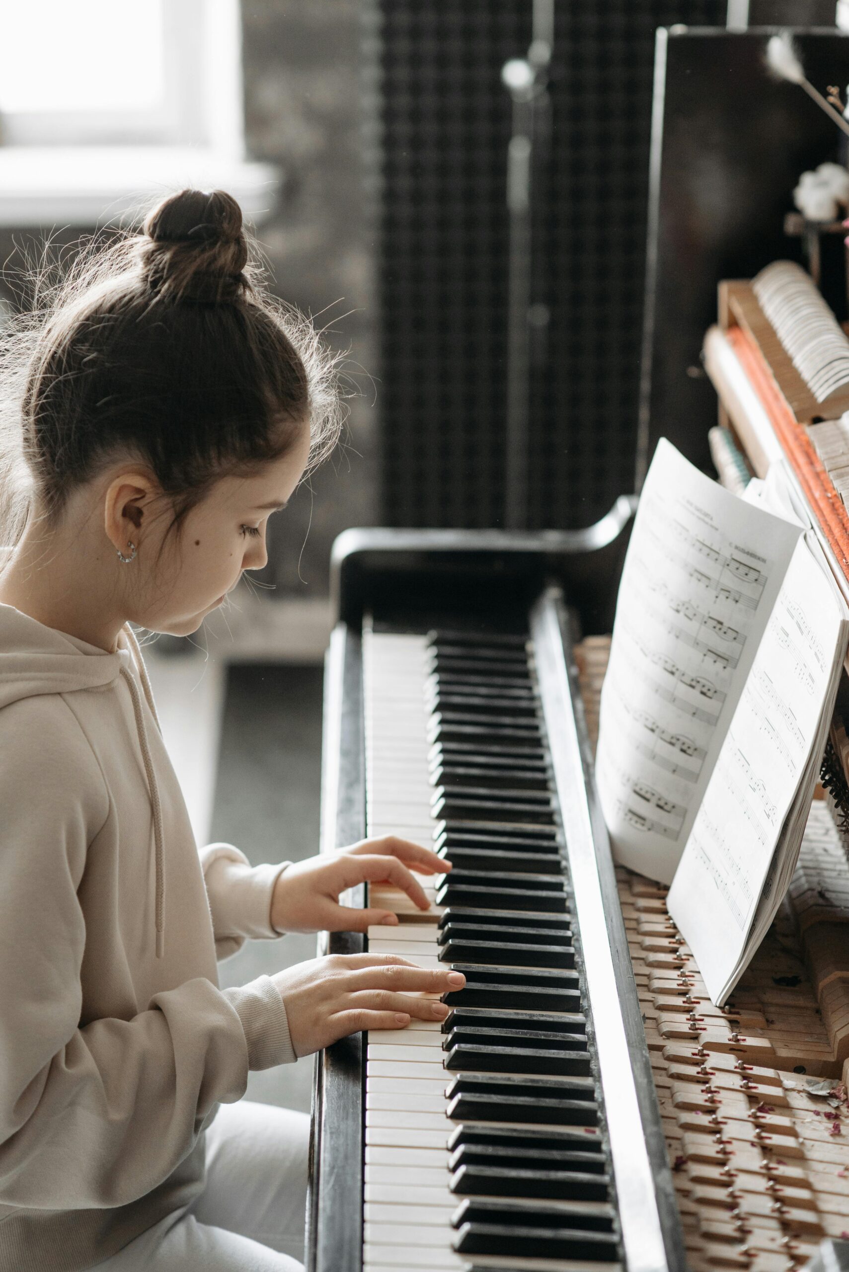 A young girl practicing piano indoors, focusing on sheet music beside her.